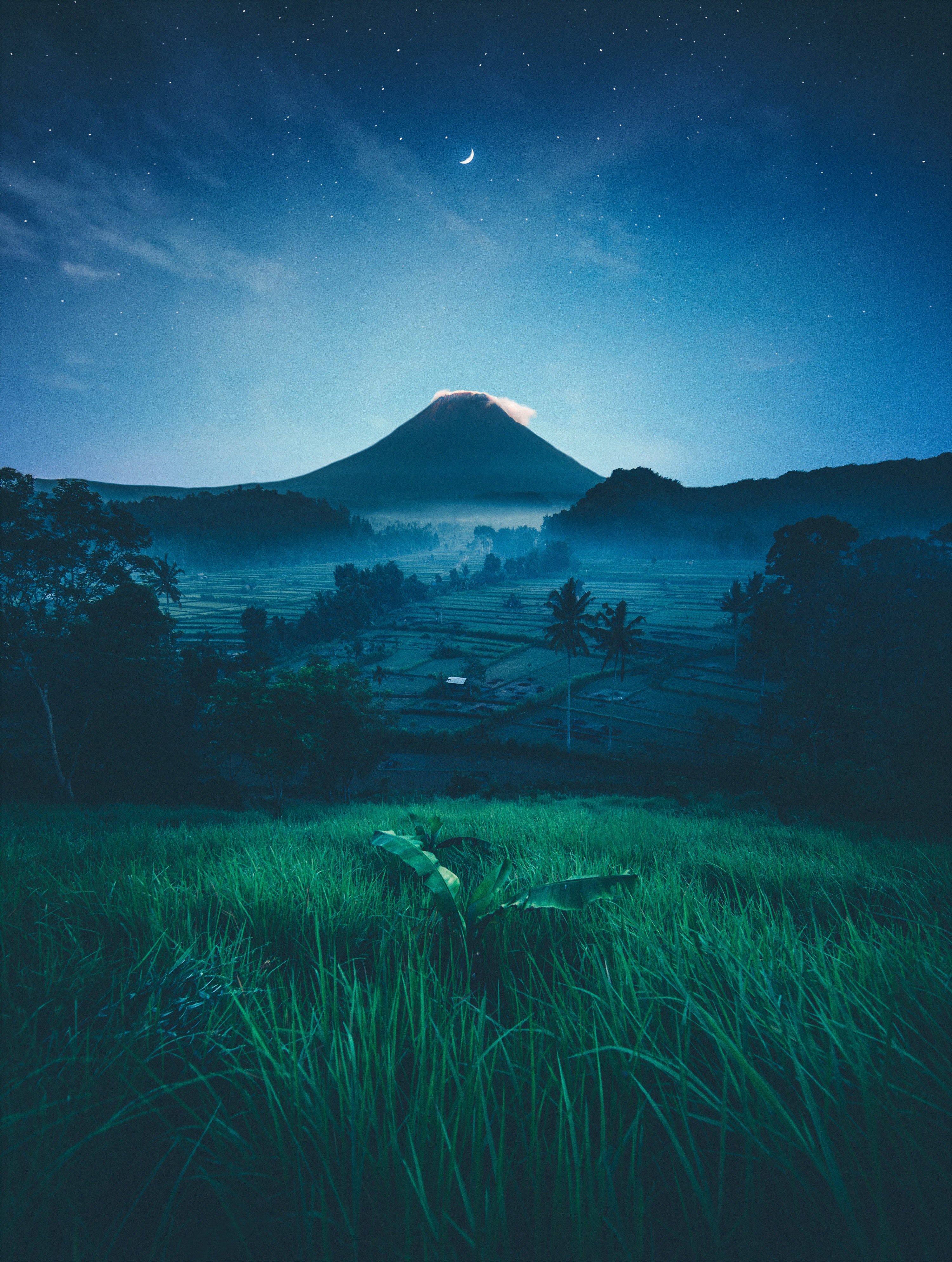 Moonlit volcano over terraced rice fields at dusk